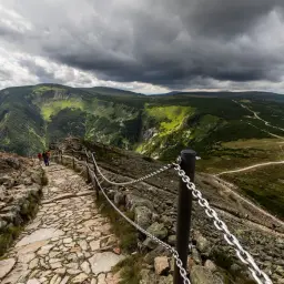 Kamienista ścieżka prowadzi na Śnieżkę. Turyści idą w górę, podziwiając krajobraz Karkonoszy.
