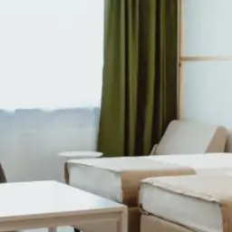 Pokój hotelowy z dwoma łóżkami, stolikiem i krzesłami. Zastanawiasz się, ile kosztuje nocleg w Warszawie?