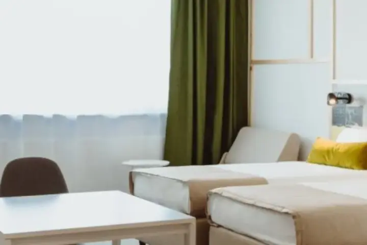 Pokój hotelowy z dwoma łóżkami, stolikiem i krzesłami. Zastanawiasz się, ile kosztuje nocleg w Warszawie?